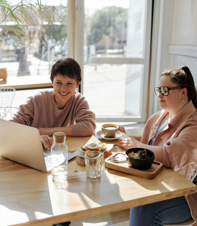 become-a-disability-advocate-auckland Woman with down syndrome working on a laptop with her advocate sitting next to her