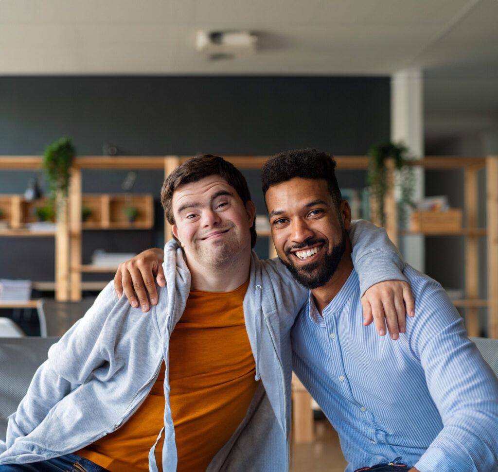 Young man with Down syndrome with his mentoring friend sitting inside