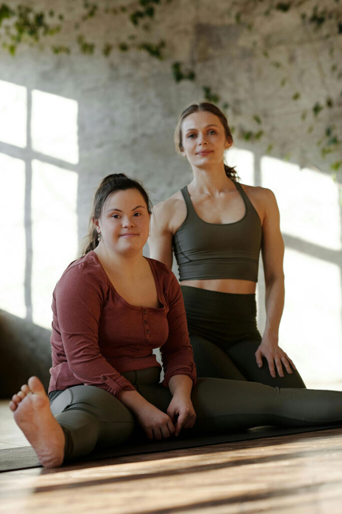 Woman with Down Syndrome and her friend sitting on the ground in a yoga pose